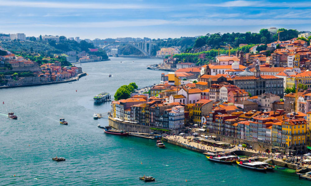 Panoramablick auf die Stadt Porto am Douro-Fluss mit bunten Gebäuden und Booten im Wasser.