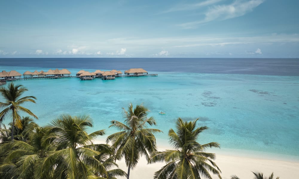 Wasserbungalows auf einer tropischen Malediveninsel, umgeben von klarem türkisem Wasser und Palmen.
