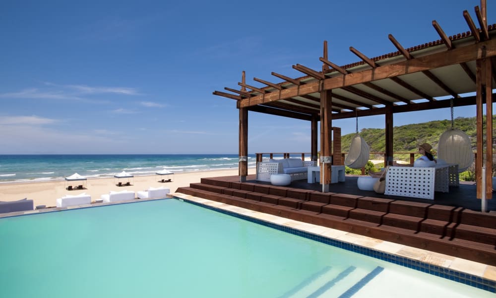 Ein luxuriöser Strandresort mit einem Pool und einer schattigen Lounge, die auf den Ozean blicken.