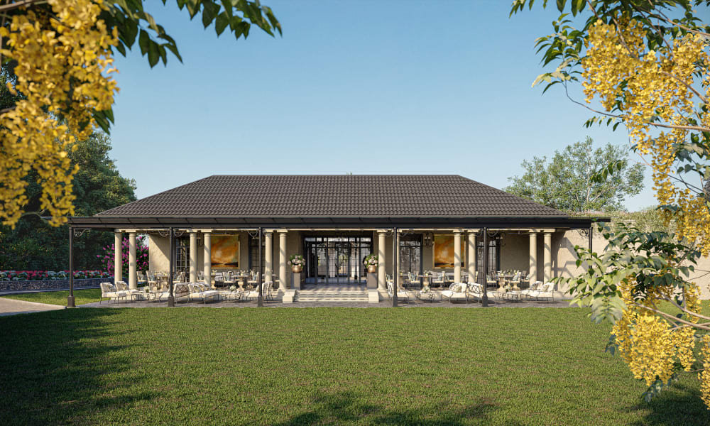Einstöckiges Haus mit großer überdachter Terrasse, die mit Tischen und Stühlen möbliert ist, umgeben von grünem Rasen und eingerahmt von blühenden Ästen unter klarem blauem Himmel.