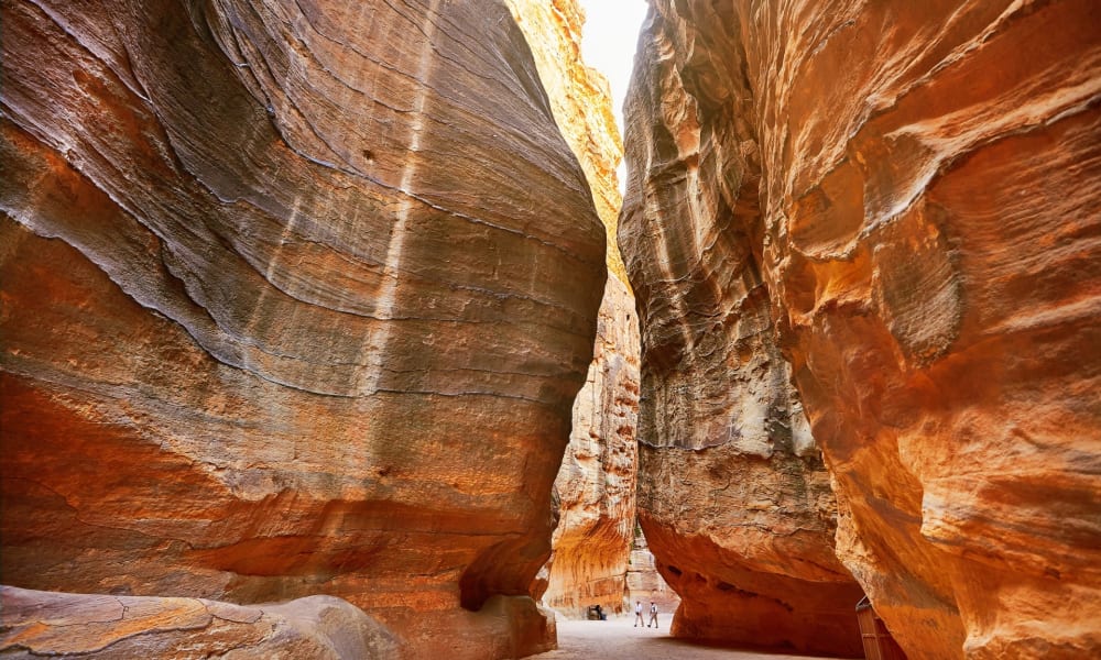 Majestöser enger Canyon mit hohen roten Felswänden und Besuchern, die auf dem sandigen Weg gehen.