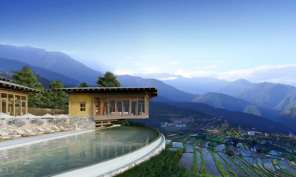 Ein modernes Gebäude mit großen Glasfenstern, das auf terrassierte Felder und Berge in Bhutan blickt.
