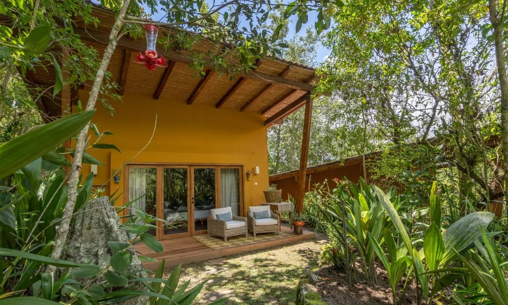 Gemütliche Sitzecke im Garten vor einem gelben Haus, umgeben von üppigem Grün.