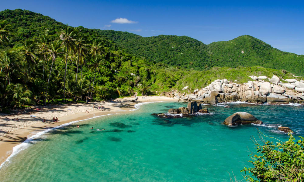 Tropischer Strand mit üppigen grünen Bergen und Palmen entlang der Küste in Kolumbien.