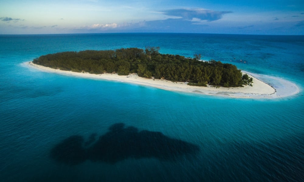 A lush green island with a sandy shoreline surrounded by blue ocean waters.