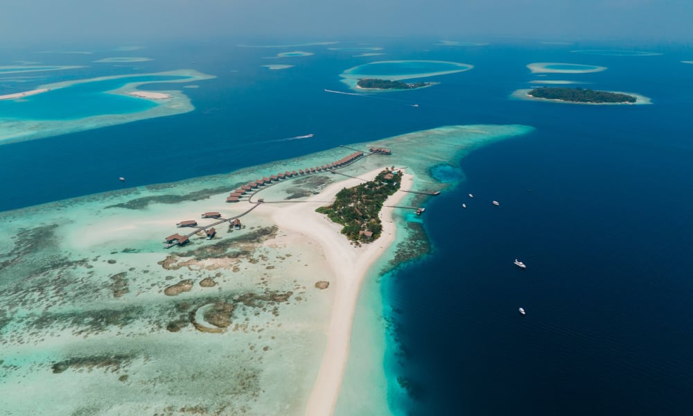 Aerial view of a tropical island with overwater bungalows, sandy beaches, and surrounding turquoise waters in the Maldives.