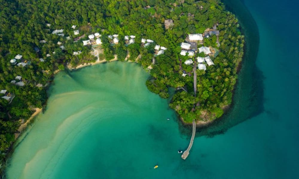 Luftaufnahme des Soneva Kiri Resorts mit Wasserbungalows, umgeben von üppigem Grün und an einer tropischen Küste gelegen.