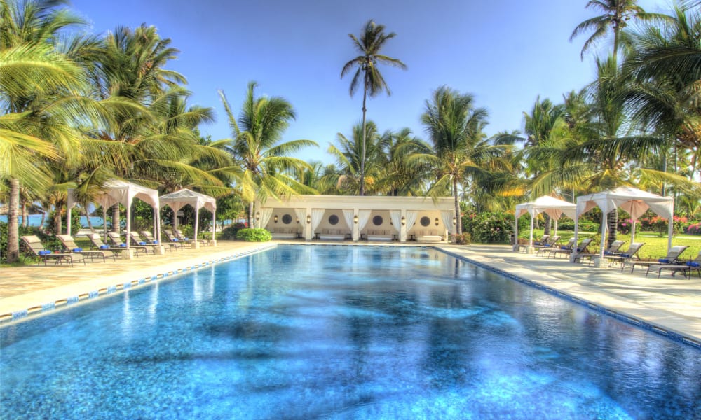 Luxuriöser Außenpool in einem tropischen Resort umgeben von Palmen und schattigen Cabanas.