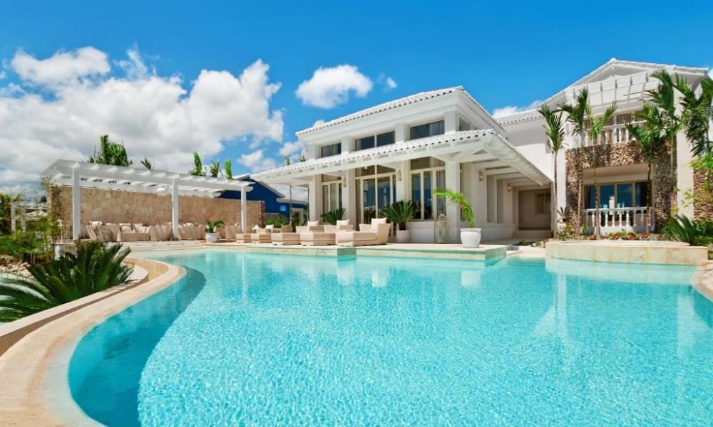 Luxusvilla mit privatem Pool, umgeben von üppigem Grün und klarem blauen Himmel.