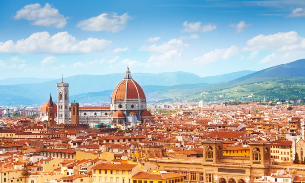 A panoramic view of Florence with the Basilica of Santa Maria del Fiore and historic buildings under a blue sky.