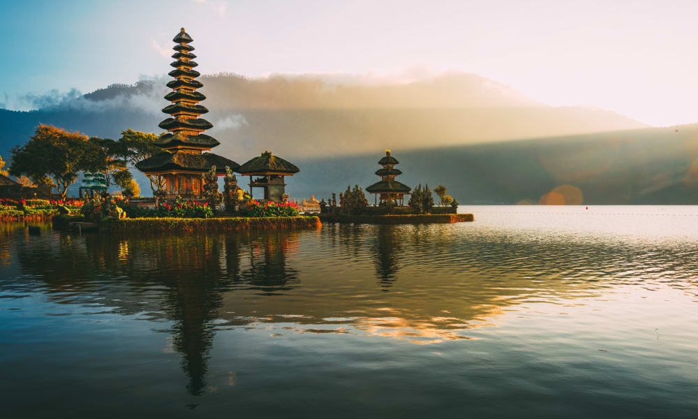 Sonnenuntergang über dem Ulun Danu-Tempel am See Bratan in Bali, Indonesien, mit Bergen, die sich im Wasser spiegeln.