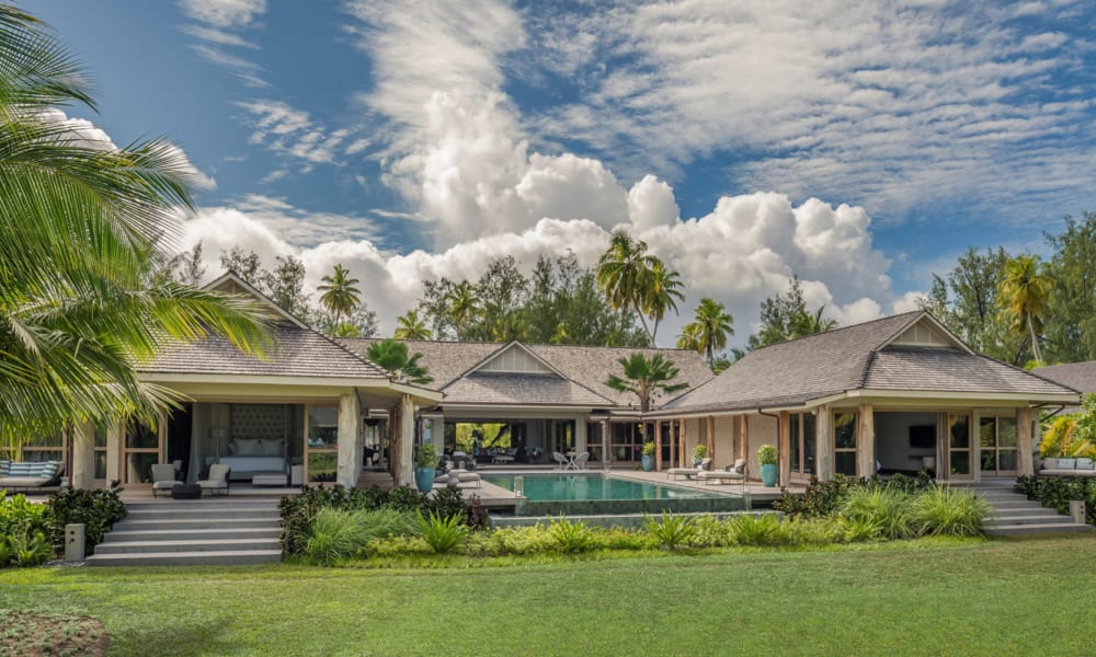 Luxuriöse dreizimmerige Präsidentenvilla im Four Seasons Resort Seychelles auf der Insel Desroches mit privatem Pool, umgeben von tropischer Vegetation unter einem wolkigen Himmel.