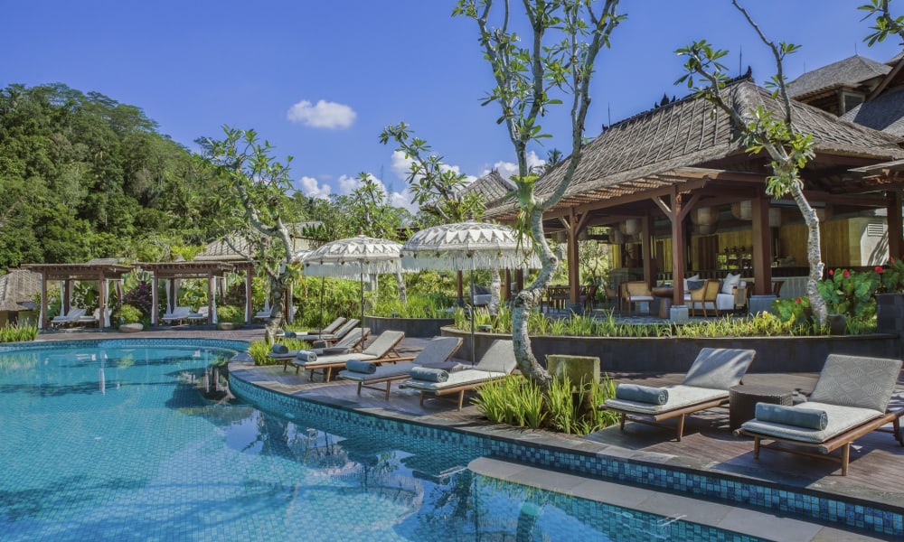 Luxuriöse Außenpoolanlage im Mandapa, a Ritz-Carlton Reserve, mit Liegestühlen, Sonnenschirmen und schattigem Sitzbereich unter Bäumen.