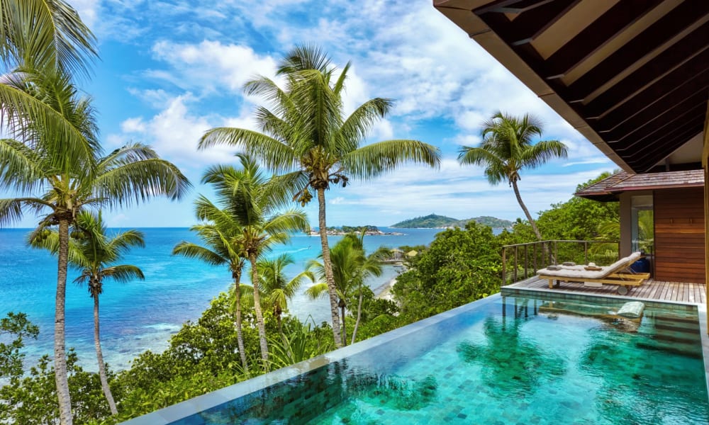 Luxus-Pool-Villa mit Meerblick, umgeben von Palmen auf einer tropischen Insel.