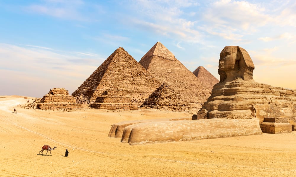 Die großen Pyramiden von Gizeh und die Sphinx in einer Wüstenlandschaft unter einem blauen Himmel.