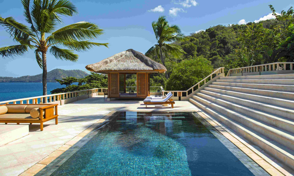 Luxushotel mit einem Pool, Liegestühlen und tropischer Umgebung mit Palmen und einem Strohdach-Pavillon.