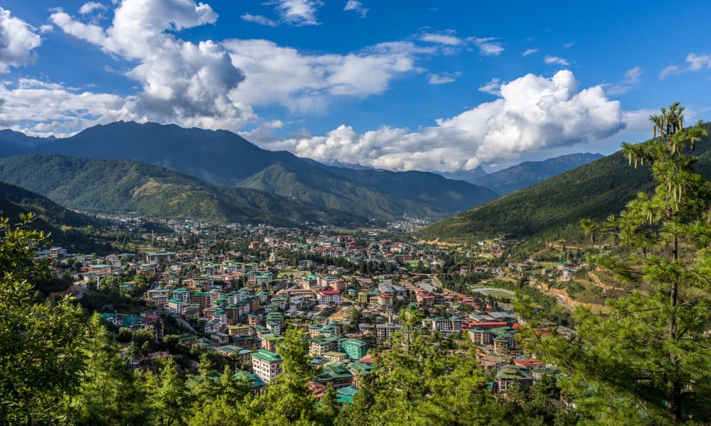 Stadtbild von Thimphu eingebettet in saftig grüne Berge unter einem partly cloudy Himmel.