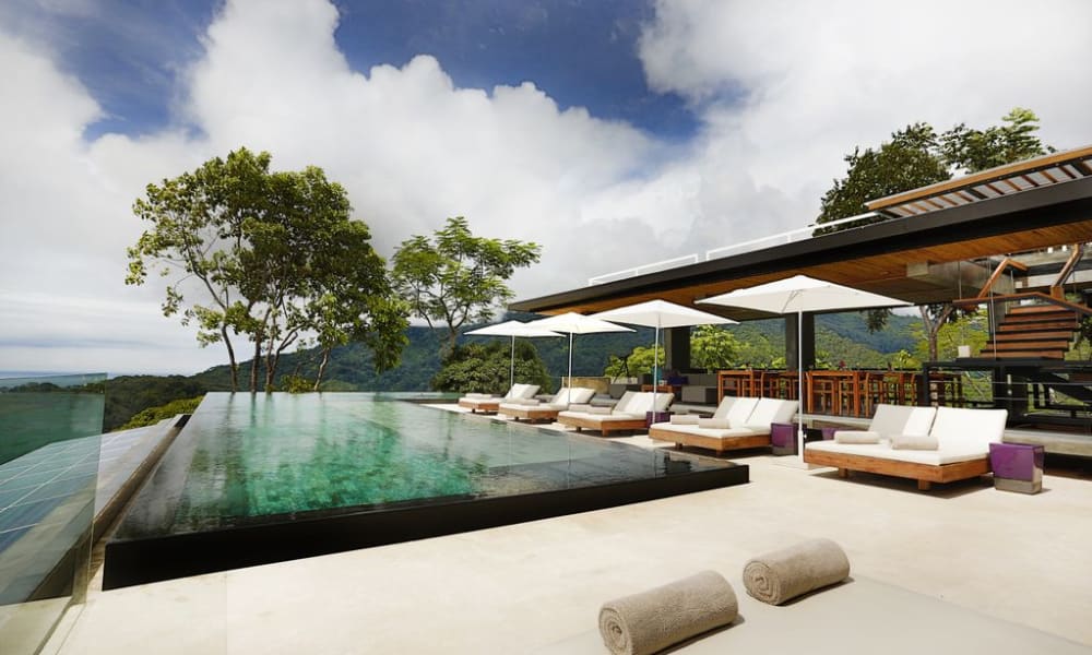 Ein luxuriöser Poolbereich im Kura Boutique Hotel in Uvita, Costa Rica, mit Sonnenliegen und Sonnenschirmen, die auf grüne Bäume und Berge blicken.