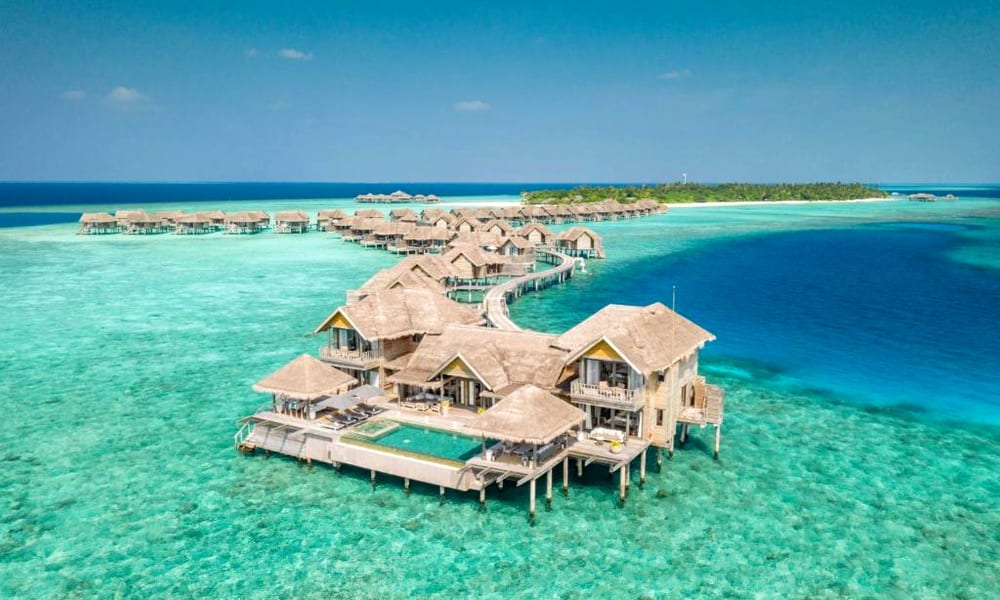 Overwater bungalows in the Maldives surrounded by turquoise waters and lush green islands in the background.