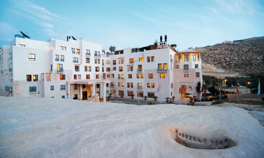 Das Moevenpick Resort Petra mit moderner weißer Architektur vor einem Hügel unter blauem Himmel.
