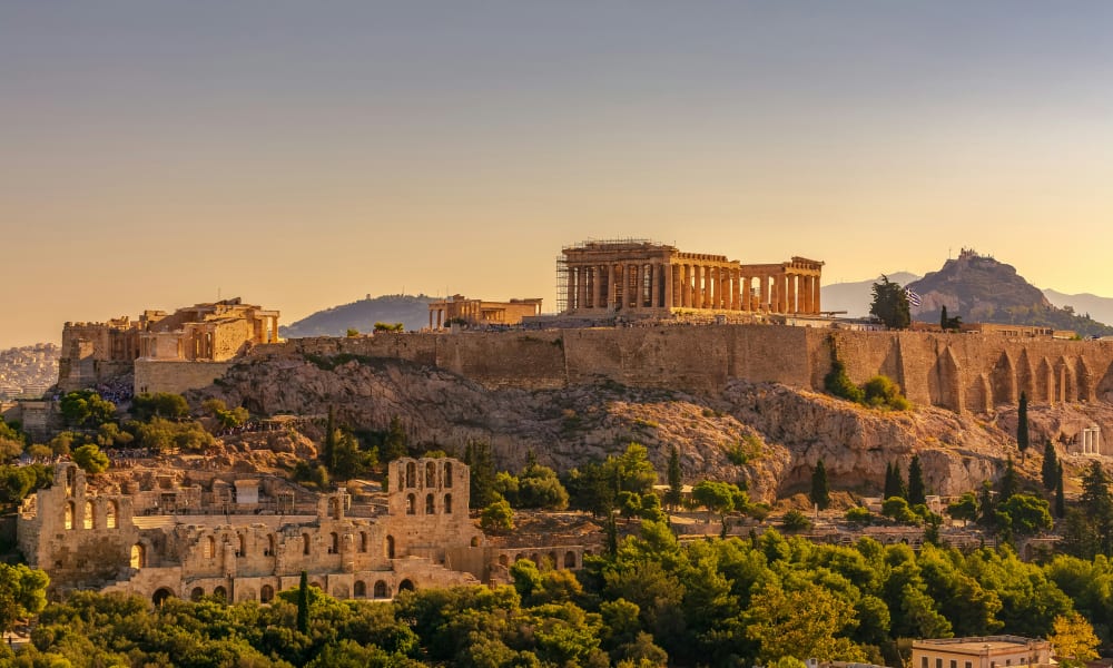 The Acropolis of Athens perched on a rocky hilltop at sunset, showcasing the ancient Parthenon temple surrounded by greenery and other historic ruins.