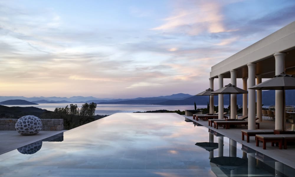 Ein Infinity-Pool mit Blick auf das Meer bei Sonnenuntergang, mit Sonnenschirmen und Liegestühlen in der Nähe.