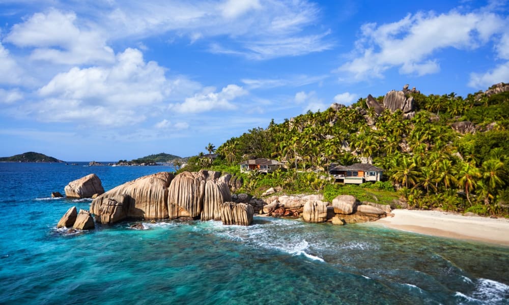 Aerial view of a tropical coastline with rocky outcrops, lush greenery, and a sandy beach on a clear day.