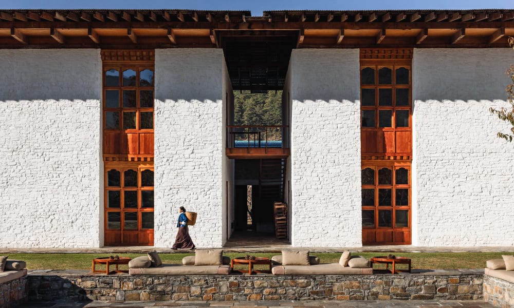 Eine Frau geht an einem traditionellen bhutanischen Gebäude mit weißen Wänden und Holzfresken vorbei.