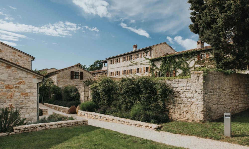 A picturesque view of the Meneghetti Wine Hotel with historic stone buildings and lush greenery in Bale, Croatia.