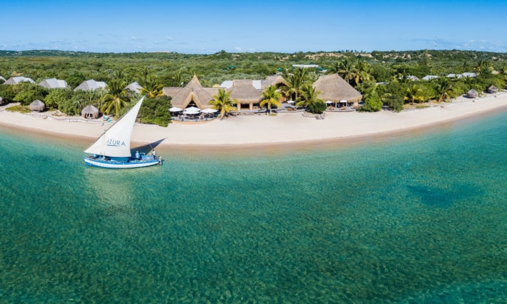 Eine Ansicht von oben auf ein luxuriöses Strandvilla-Resort auf Benguerra Island mit einem Segelboot in der Nähe und üppiger grüner Umgebung.