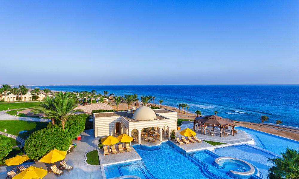 A luxurious resort with multiple pools and yellow umbrellas overlooking the ocean in Egypt.