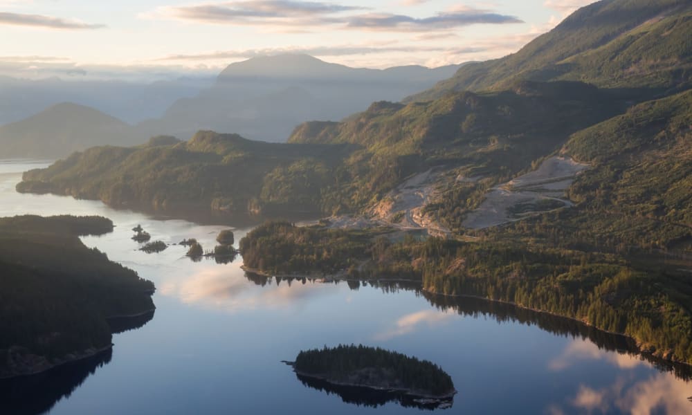 Eine ruhige Landschaft mit einem stillen Fluss, der durch grüne Hügel und Berge während des Sonnenuntergangs fließt.