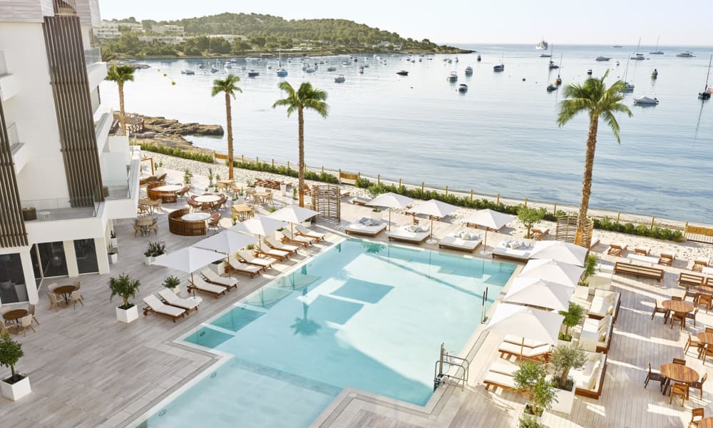 Luxuspool im Hotel mit Sonnenliegen, Sonnenschirmen und Palmen mit Blick auf einen Yachthafen in Ibiza, Spanien.