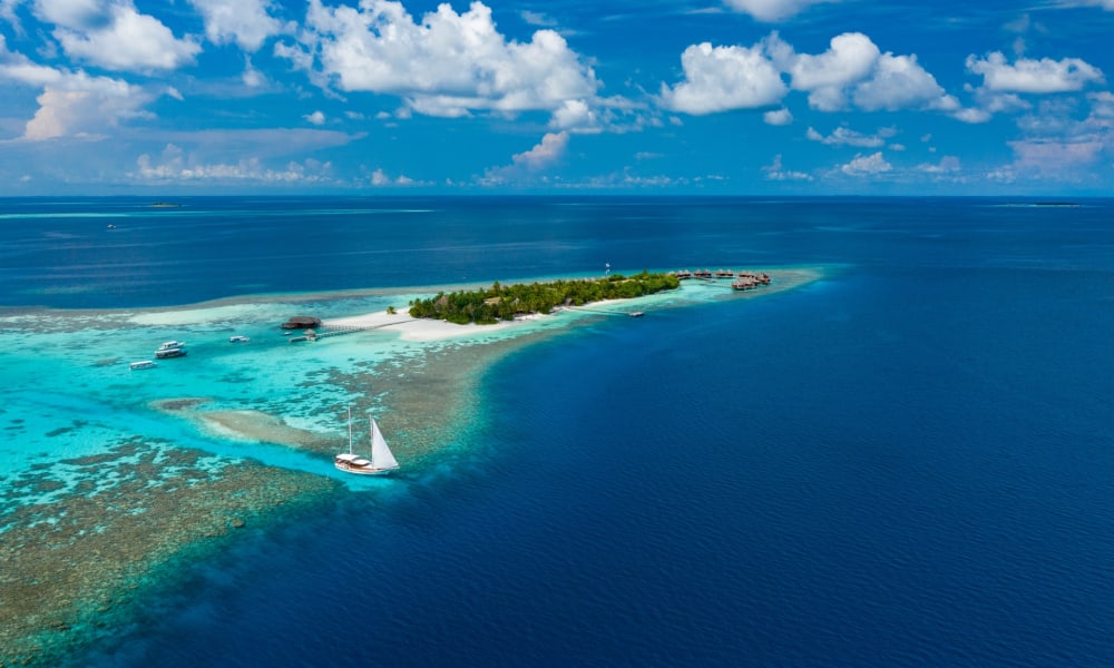 Ein Luftbild vom Mirihi-Insel-Resort mit klarem blauen Wasser, einem Sandstrand und dichter Vegetation.