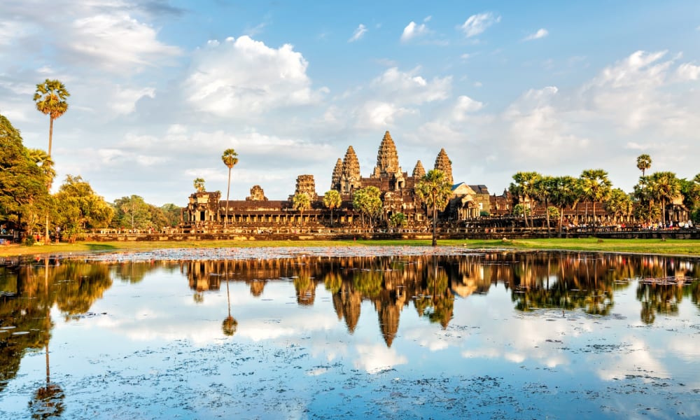 Angkor Wat Tempelkomplex spiegelt sich in einem großen Teich mit blauem Himmel und vereinzelten Wolken.