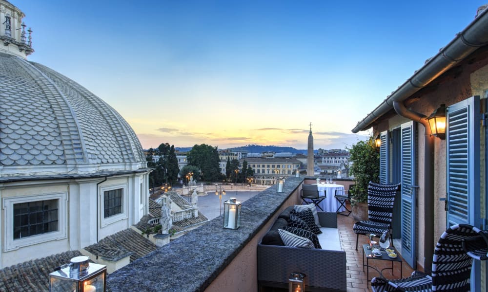 Dachterrasse mit Sitzgelegenheiten und Laternen, mit Blick auf historische Gebäude bei Sonnenuntergang.