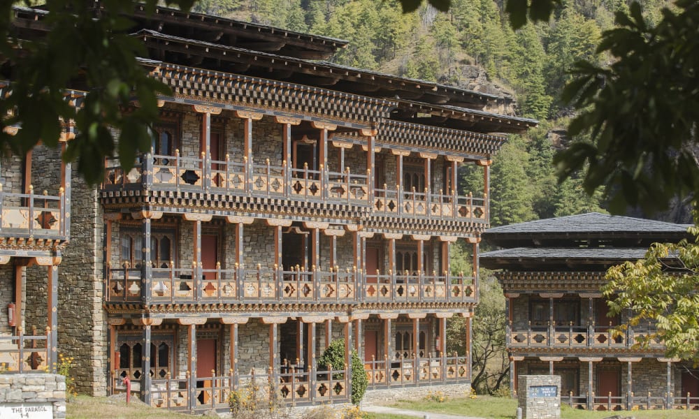 Traditional multi-story building with intricate wooden balconies, surrounded by greenery in a hilly landscape.