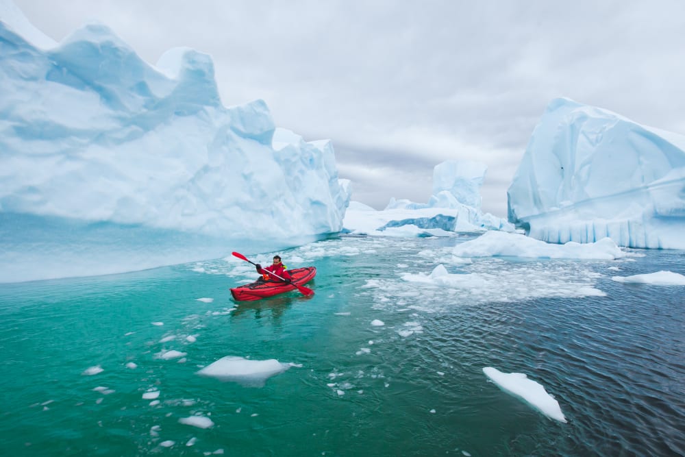 A person kayaking through icy waters surrounded by large icebergs in Antarctica.