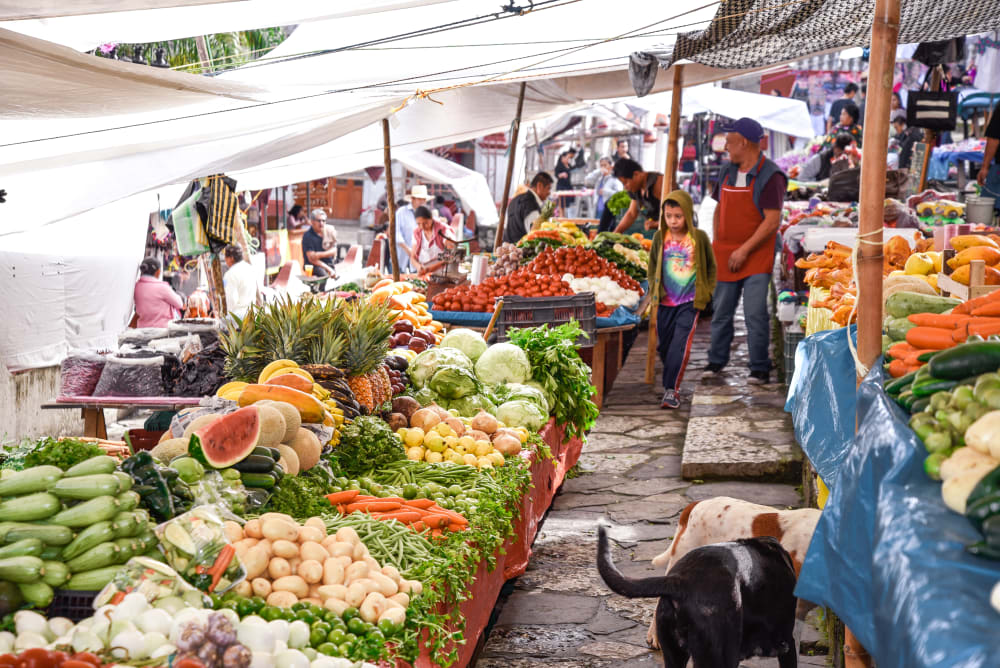 Belebter Außenmarkt in Cuetzalan, Mexiko, mit frischem Obst und Gemüse auf Tischen unter weißen Markisen und Menschen, die die Stände besuchen.