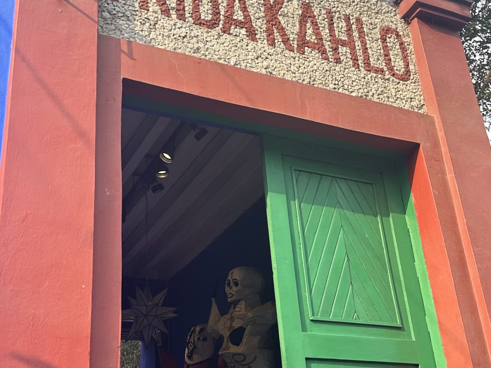 Entrance of the Frida Kahlo Museum in Mexico City with a partially open green door and visible skeleton figurines inside the building framed by red walls.