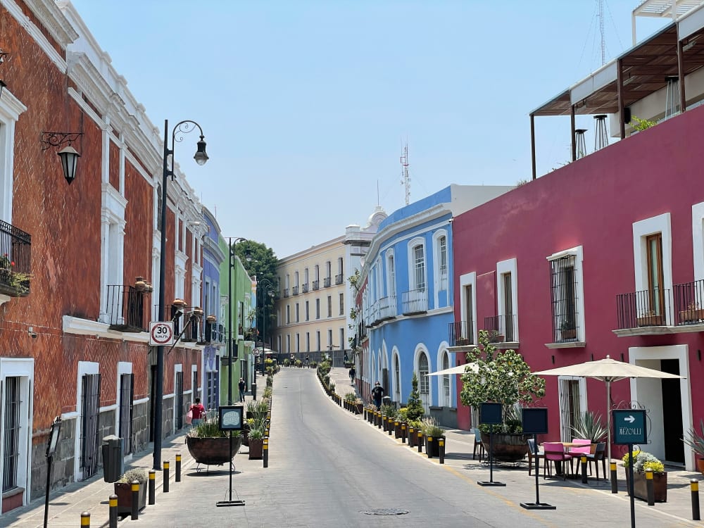 Ruhige Straße in Puebla, Mexiko, gesäumt von bunten kolonialstil Häusern mit roten, grünen, blauen und violetten Fassaden unter klarem blauem Himmel.