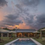 Ein luxuriöses Haus mit einem Schwimmbecken im Freien, umgeben von Liegestühlen und Sonnenschirmen beim Sonnenuntergang.
