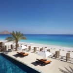 Ein luxuriöses Strandresort mit einem Swimmingpool, weißem Sandstrand, Palmen und Sonnenliegen mit Sonnenschirmen mit Blick auf den Ozean.
