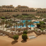 Ein luxuriöses Wüstenresort mit einem Pool, umgeben von Palmen und Sonnenliegen, in einer trockenen Wüstenumgebung.