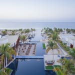 Ein luxuriöser Ferienort am Meer mit einem Pool, Palmen, Liegestühlen und Blick auf den Ozean im Hintergrund.