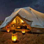 Ein Leinentent unter einem sternenklaren Nachthimmel in einer Wüste, von innen beleuchtet.