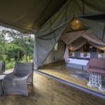 Luxurious tent interior with a bed and seating area overlooking a lush green landscape.