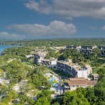 Luftaufnahme des Sofitel Baru Resorts an einer üppig grünen Küste mit modernen Gebäuden, türkisem Meer, Sandstrand und teils bewölktem Himmel.