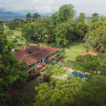 Luftaufnahme der Hacienda Bambusa, umgeben von dichtem grünem Baumbestand und Vegetation mit einem klaren Hof und bewölktem Himmel im Hintergrund.