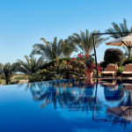 Infinity-Pool im Lazib Inn Resort & Spa mit Palmen, Liegestühlen, Sonnenschirmen und klarem blauem Himmel.